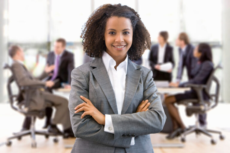 A young business professional standing confidently with her team in the background.