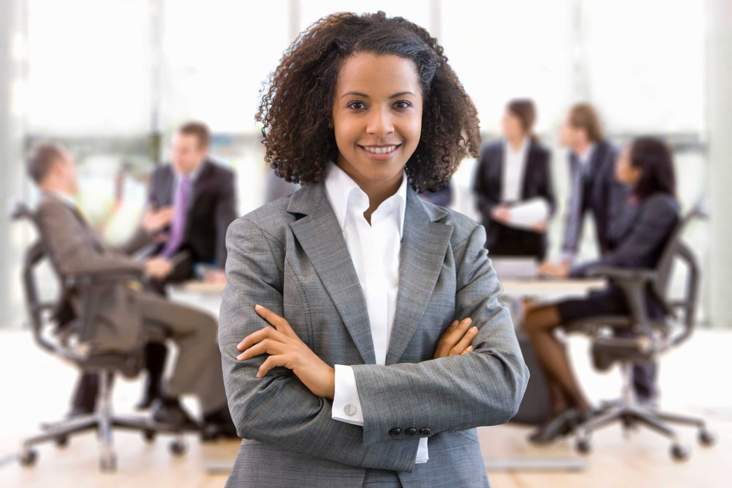 A young business professional standing confidently with her team in the background.