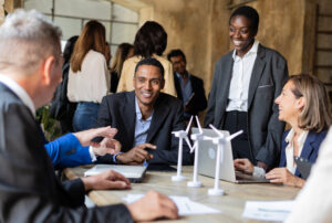 Multiracial group of business professionals at a meeting, with laptops and small models of wind turbines on top of a table.