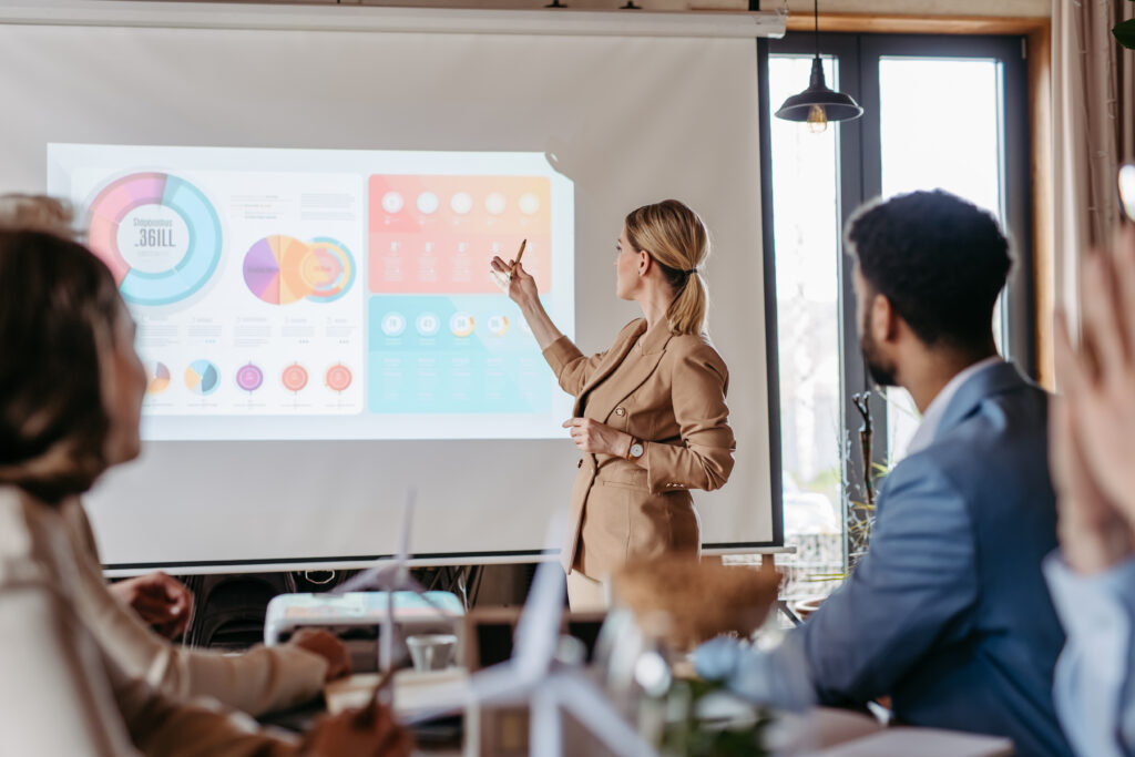 A business professional presenting pie charts and graphs on a large screen.