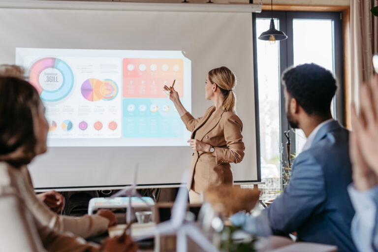 A business professional presenting pie charts and graphs on a large screen.
